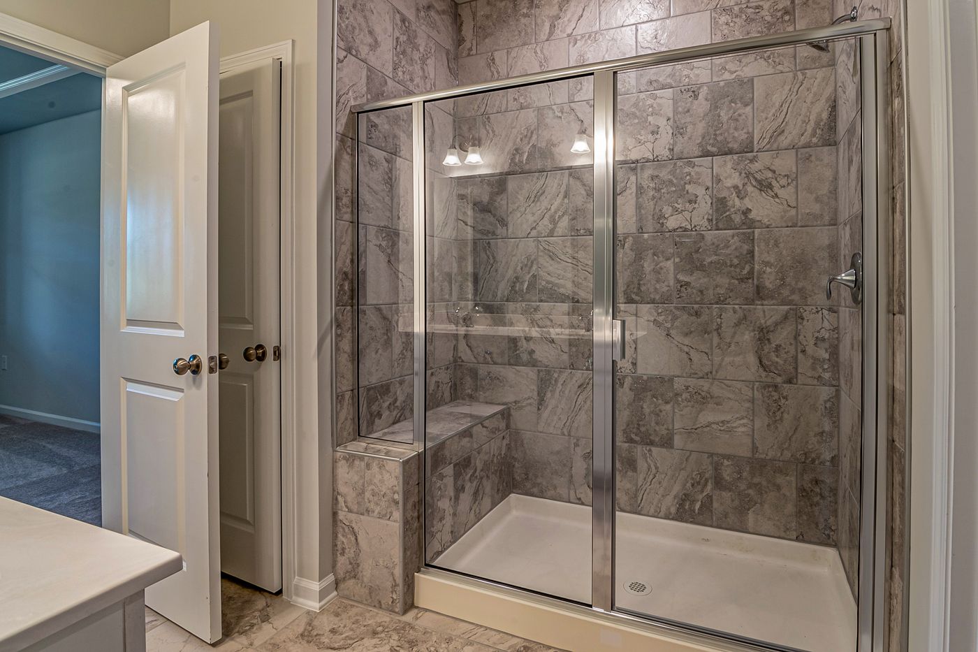 A remodeled bathroom with a frameless glass shower and marble tile